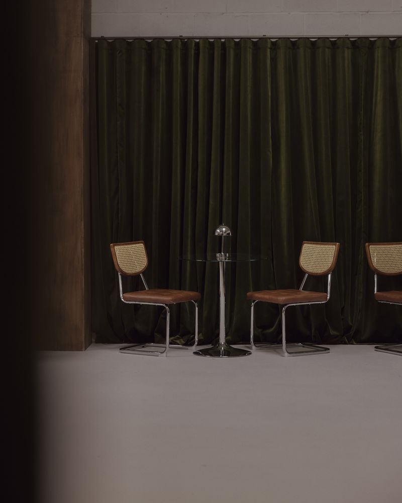 Cane chairs and a glass table in front of the olive velvet curtain set.