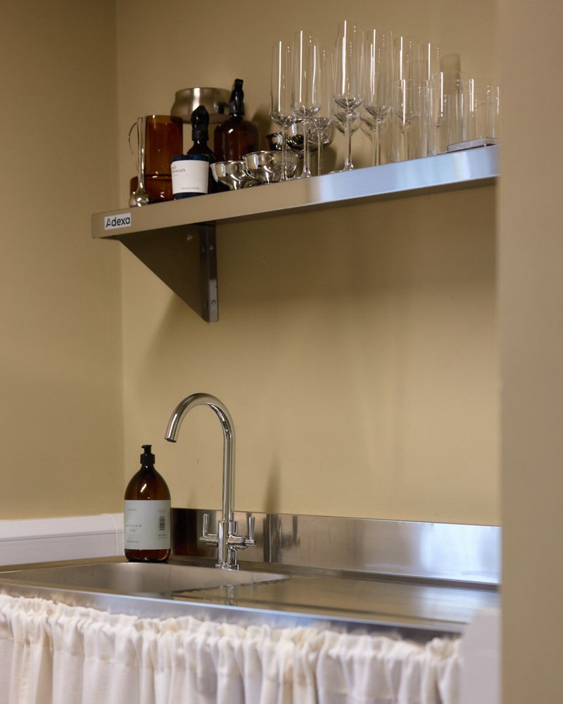 Studio kitchenette with stainless steel sink, glassware shelf and soft curtain under-counter.